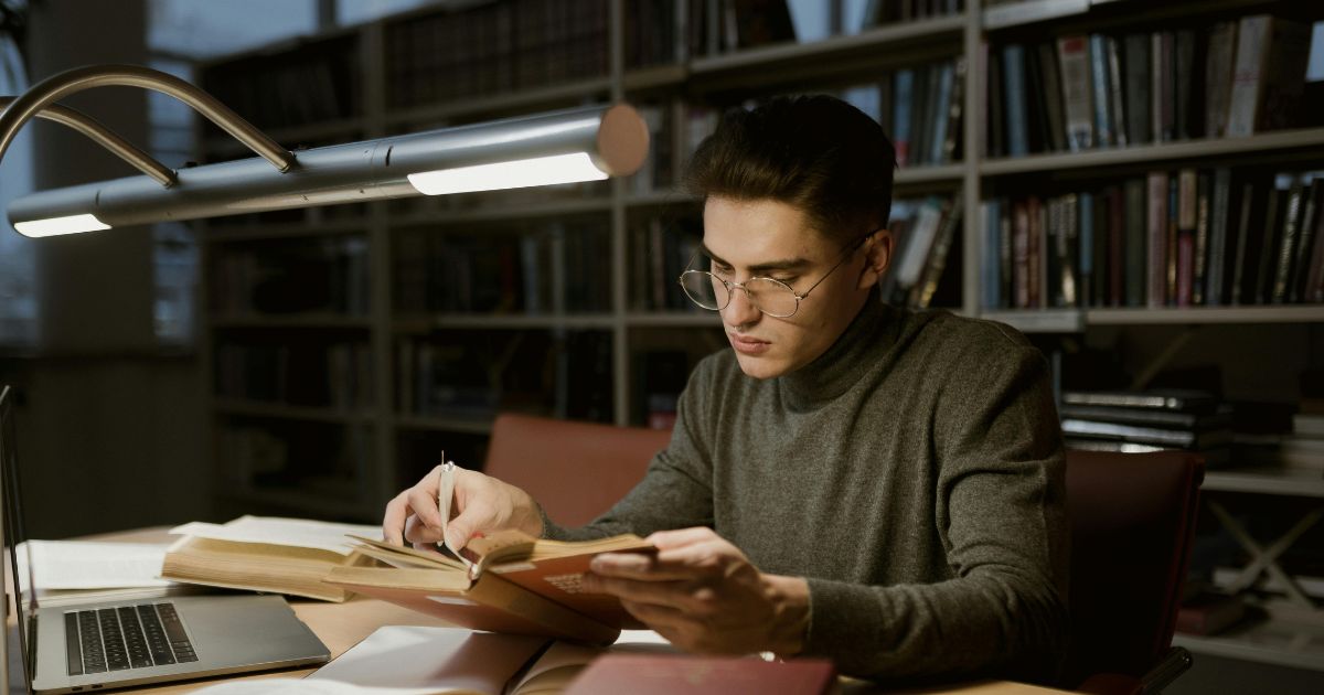 A young scholar studying in the library with books and a laptop, representing dedication and commitment to the Leo Baeck Fellowship.