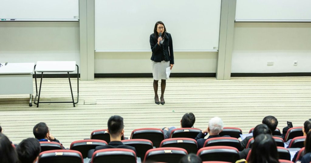 Female speaker addressing an audience in a university lecture hall, representing an academic setting related to Cox MBA Scholarships.