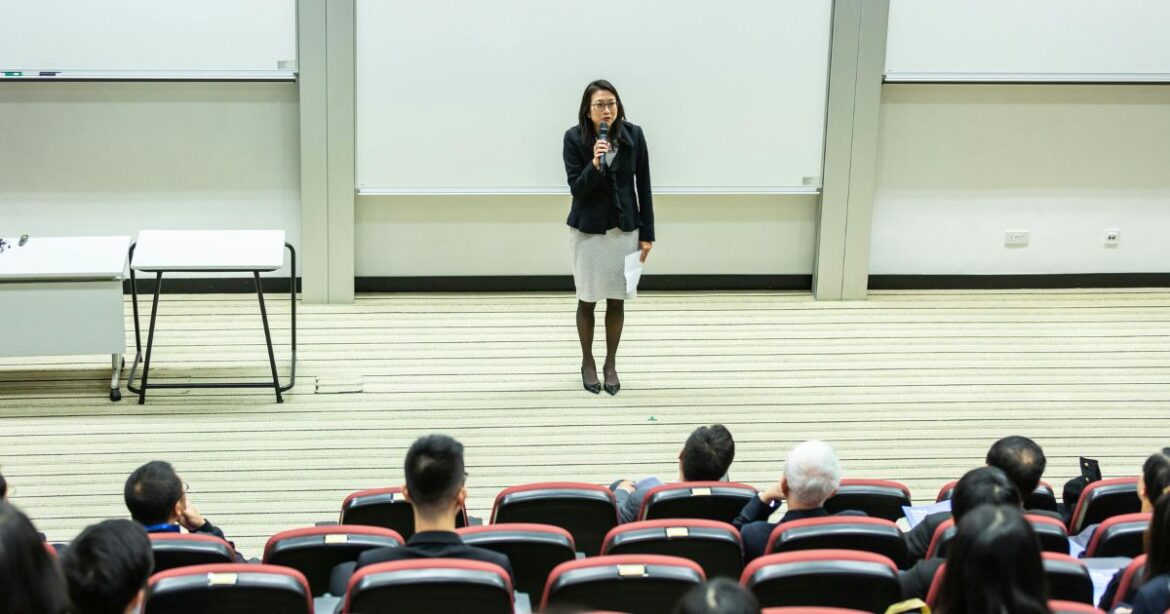 Cox Full-Time Two-Year MBA Scholarships Female speaker addressing an audience in a university lecture hall, representing an academic setting related to Cox MBA Scholarships.