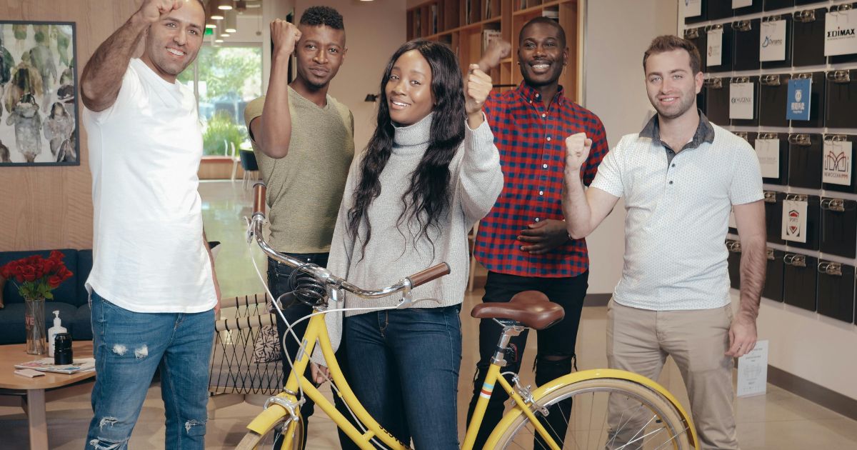 A diverse group of young professionals posing with a yellow bicycle, celebrating their journey with the Dream Together Master's Scholarship.