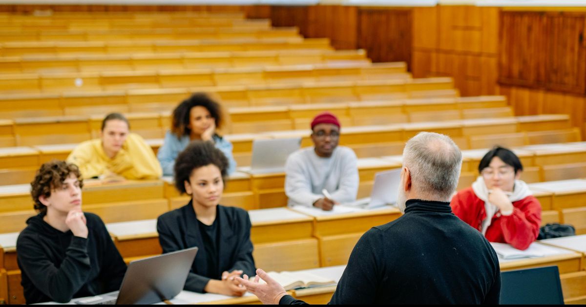 Alt text: A professor addressing a group of students in a lecture room. This represents academic opportunities and excellence like the Chancellor's Scholarship.