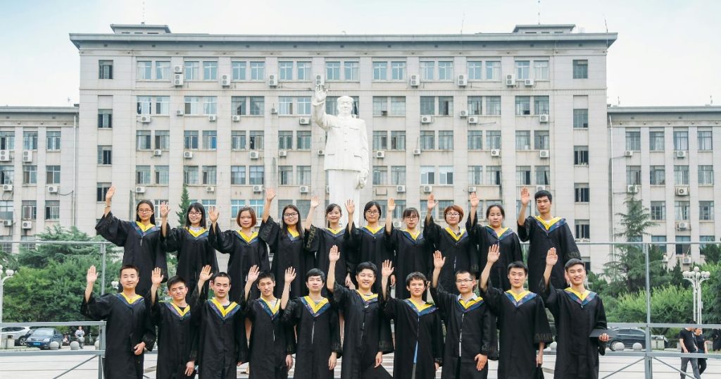 Group of university graduates in black gowns posing in front of a statue, celebrating their achievement under the Link Scholarship program.