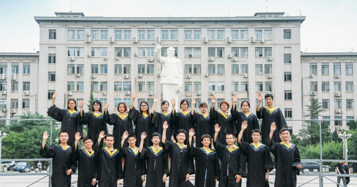LINK SCHOLARSHIP Group of university graduates in black gowns posing in front of a statue, celebrating their achievement under the Link Scholarship program.