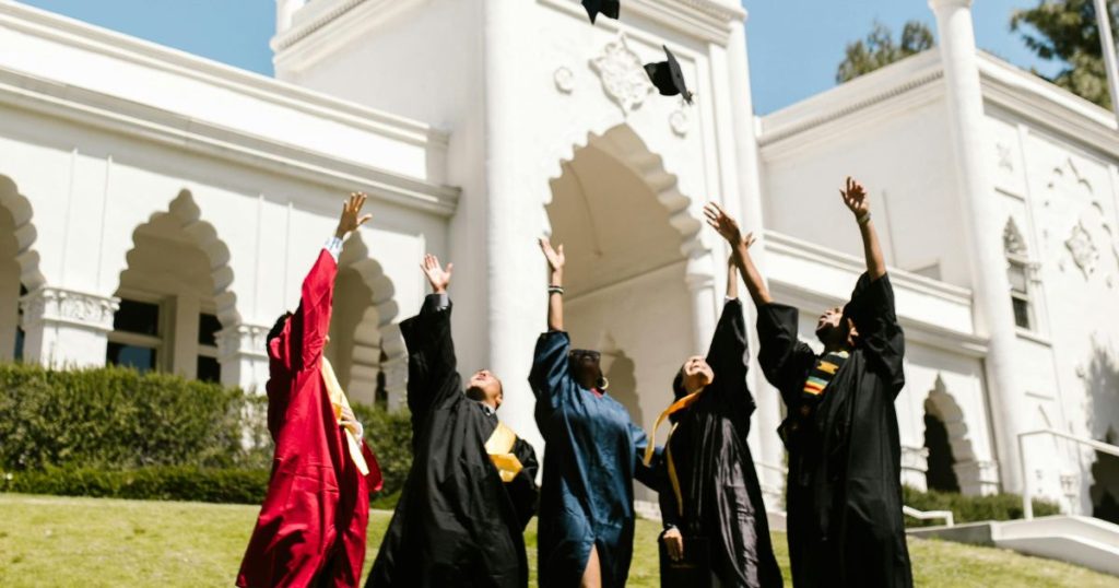 Graduates celebrating their success by tossing caps in the air in front of a grand university building, symbolizing academic achievement and opportunities like the Concordia University Presidential Scholarship.