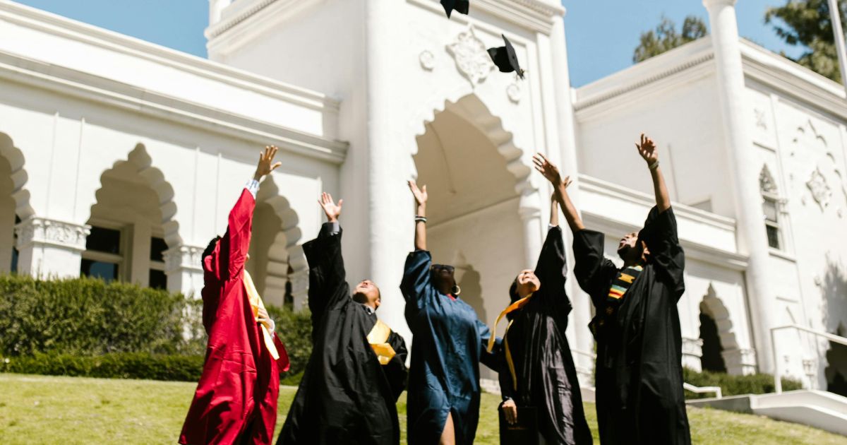 Graduates celebrating their success by tossing caps in the air in front of a grand university building, symbolizing academic achievement and opportunities like the Concordia University Presidential Scholarship.