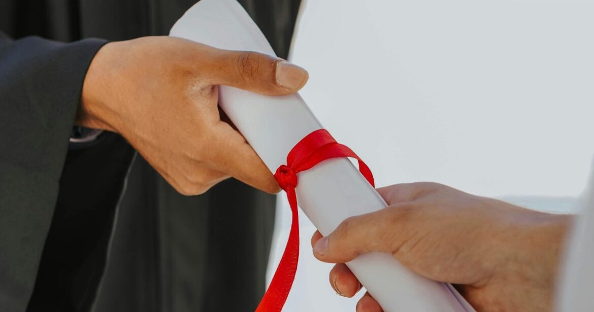 EBS Scholarship Close-up of a graduate receiving a certificate tied with a red ribbon, symbolizing academic achievement and opportunities like the EBS Scholarship.