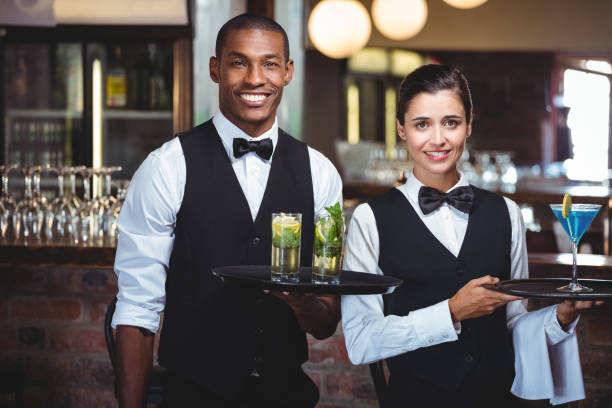 Portrait of waiter and waitress holding a serving tray with glass of cocktail Wait Staff